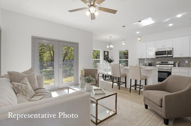 living room featuring french doors, ceiling fan with notable chandelier, light hardwood / wood-style floors, and plenty of natural light