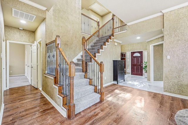 entryway with a towering ceiling, wood-type flooring, and ornamental molding