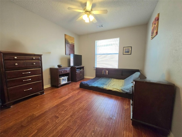 bedroom with a textured ceiling, ceiling fan, and dark wood-type flooring