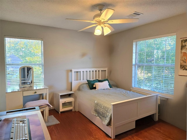 bedroom with dark hardwood / wood-style flooring, ceiling fan, multiple windows, and a textured ceiling