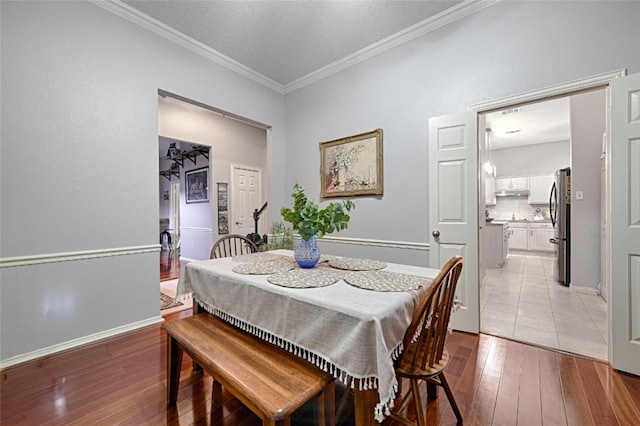 dining area featuring light hardwood / wood-style floors, ornamental molding, and a textured ceiling