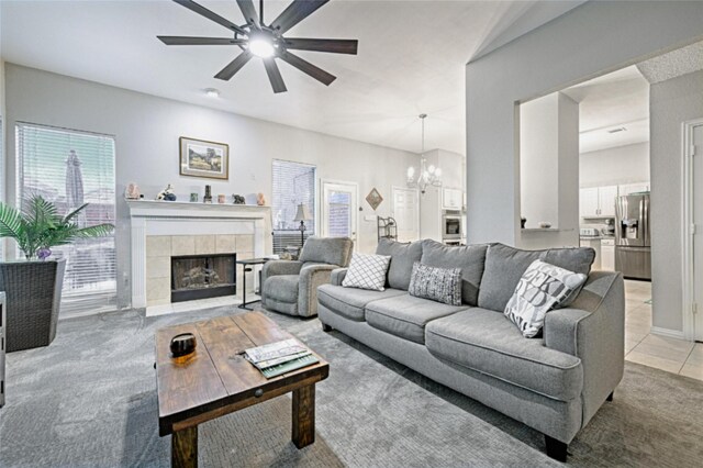 carpeted living room with ceiling fan with notable chandelier and a tile fireplace