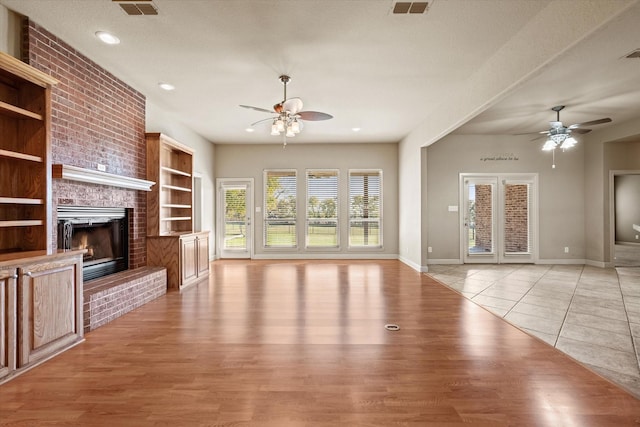 unfurnished living room with a textured ceiling, a fireplace, light hardwood / wood-style floors, and built in features