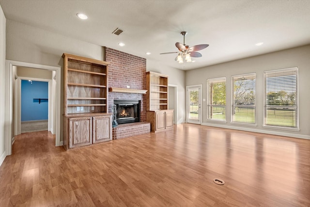 unfurnished living room featuring ceiling fan, light hardwood / wood-style floors, a textured ceiling, and a brick fireplace