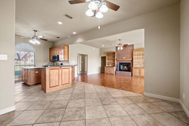 kitchen featuring kitchen peninsula, light wood-type flooring, a brick fireplace, ceiling fan, and a center island