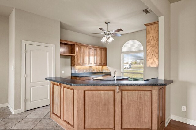 kitchen with kitchen peninsula, ceiling fan, light tile patterned flooring, and decorative backsplash