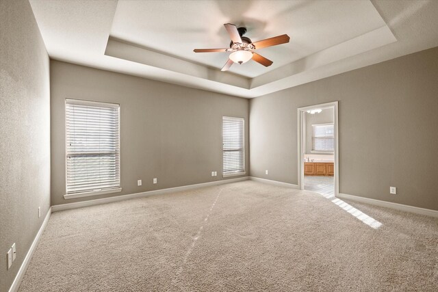 carpeted empty room with a tray ceiling, plenty of natural light, and ceiling fan