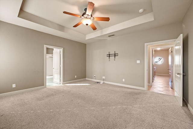 spare room with a raised ceiling, ceiling fan, and light carpet