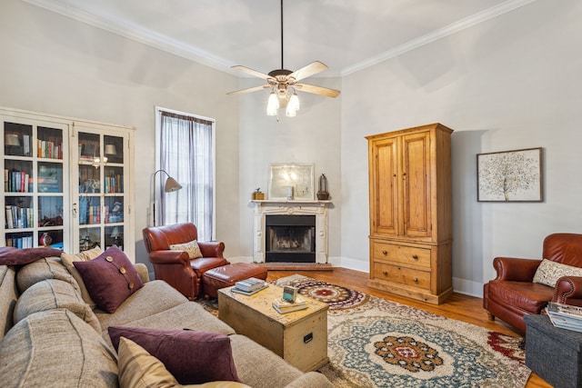 living room featuring ceiling fan, light wood-type flooring, ornamental molding, and a towering ceiling