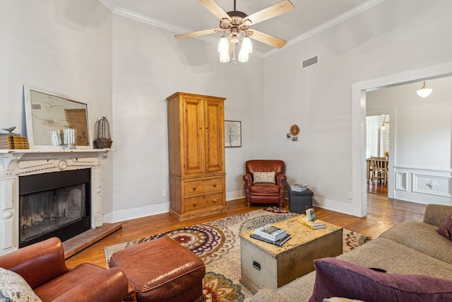 living room featuring ceiling fan, ornamental molding, a high ceiling, and light hardwood / wood-style flooring