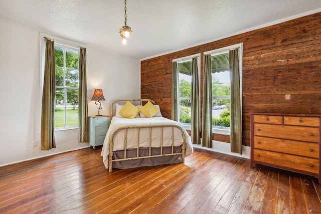 bedroom with wooden walls, a textured ceiling, and hardwood / wood-style flooring