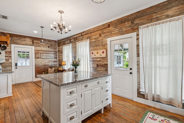 kitchen with wooden walls, decorative light fixtures, white cabinets, hardwood / wood-style floors, and a center island