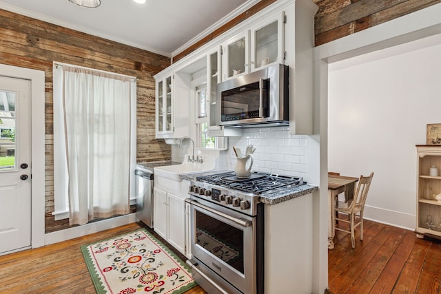 kitchen featuring white cabinetry, a healthy amount of sunlight, stainless steel appliances, tasteful backsplash, and wooden walls