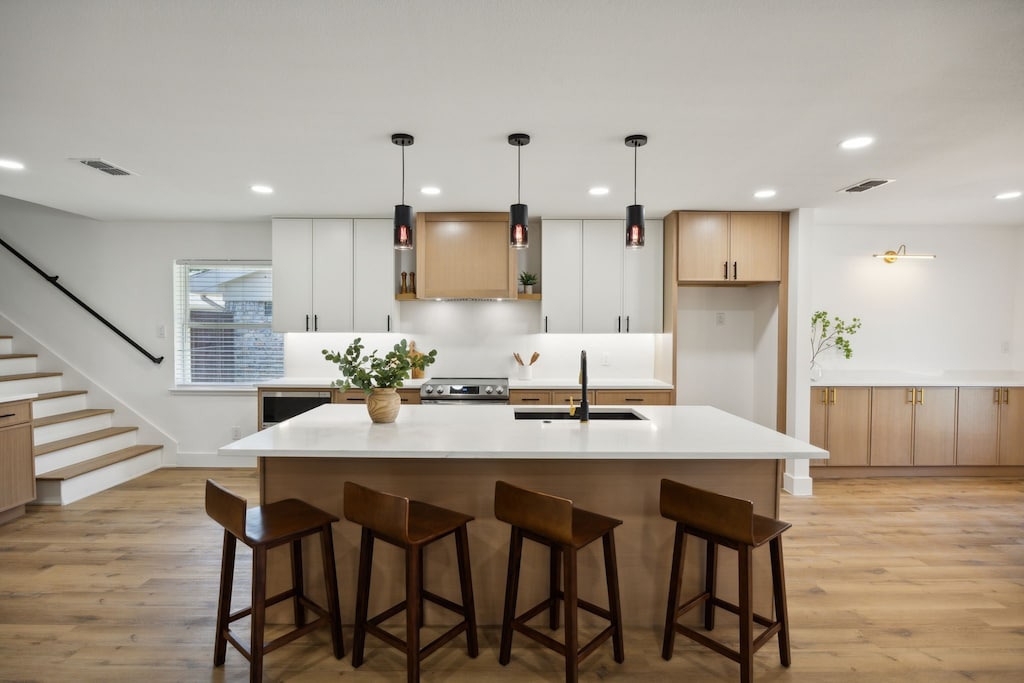 kitchen with white cabinets, pendant lighting, light wood-type flooring, and sink