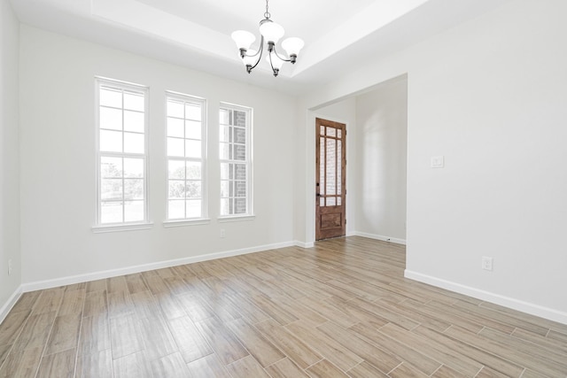 empty room with a raised ceiling, light hardwood / wood-style floors, and a notable chandelier