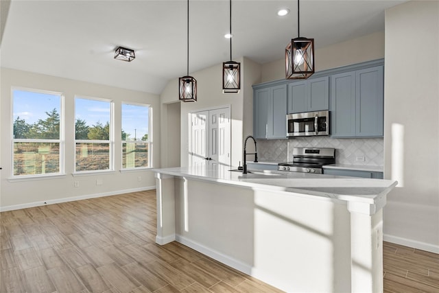 kitchen featuring appliances with stainless steel finishes, tasteful backsplash, an island with sink, sink, and hanging light fixtures