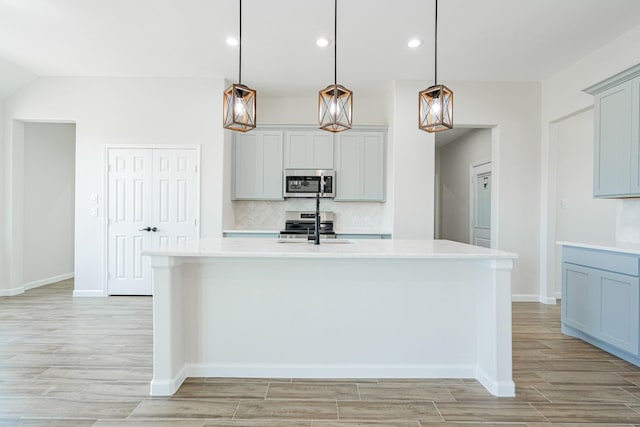 kitchen with sink, appliances with stainless steel finishes, a kitchen island with sink, hanging light fixtures, and tasteful backsplash