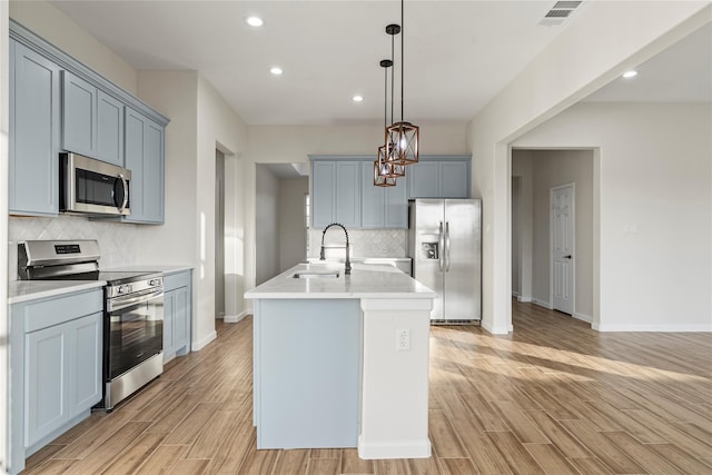 kitchen with sink, appliances with stainless steel finishes, light hardwood / wood-style floors, an island with sink, and decorative light fixtures