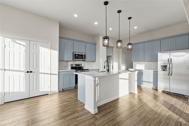 kitchen featuring sink, hanging light fixtures, backsplash, stainless steel appliances, and a center island with sink