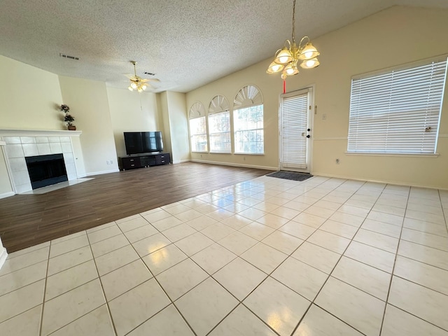 unfurnished living room with a tile fireplace, light hardwood / wood-style flooring, a textured ceiling, vaulted ceiling, and ceiling fan with notable chandelier