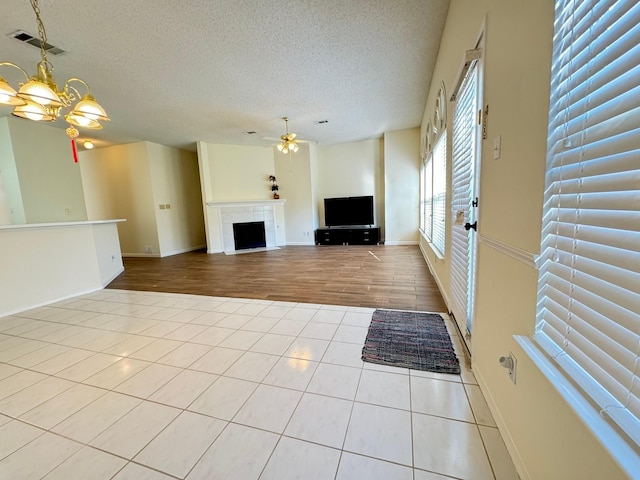 unfurnished living room featuring ceiling fan with notable chandelier, a textured ceiling, and light tile patterned floors