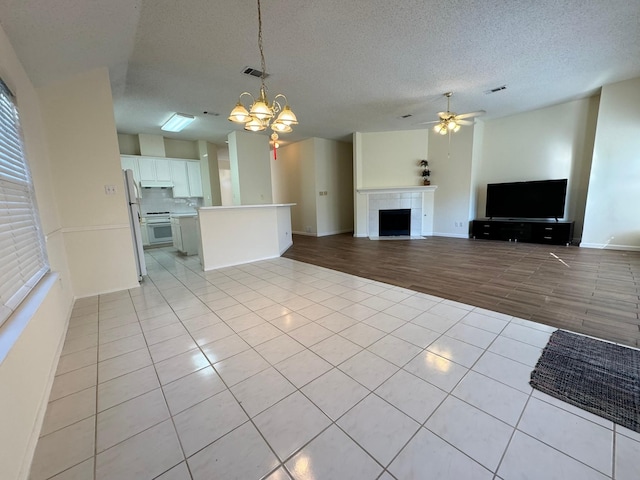 unfurnished living room featuring a textured ceiling, a tiled fireplace, ceiling fan with notable chandelier, and light wood-type flooring