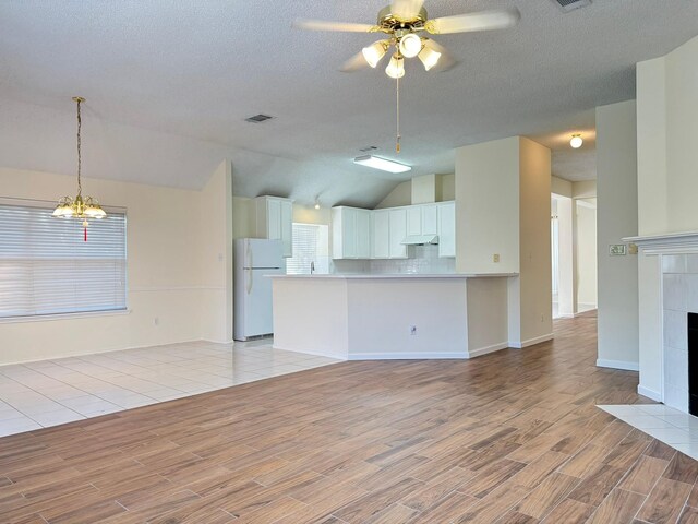 unfurnished living room with lofted ceiling, ceiling fan with notable chandelier, light hardwood / wood-style flooring, a textured ceiling, and a fireplace