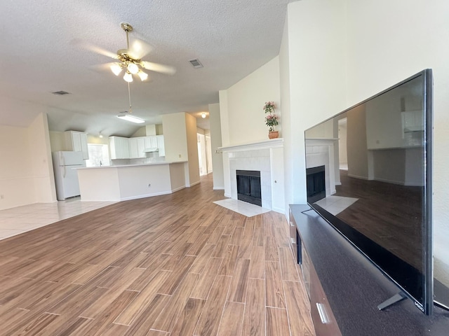 unfurnished living room with vaulted ceiling, a textured ceiling, and ceiling fan