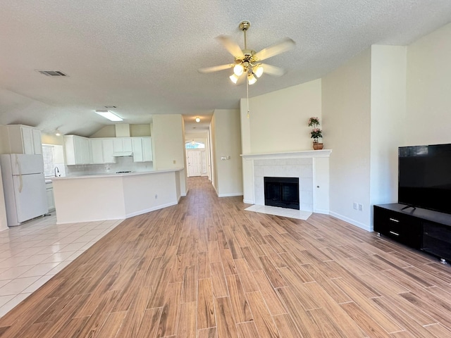 unfurnished living room with a textured ceiling, light wood-type flooring, vaulted ceiling, and a tiled fireplace