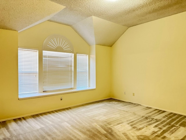 carpeted empty room featuring a textured ceiling and vaulted ceiling