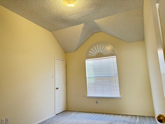 unfurnished room with a textured ceiling, light carpet, and vaulted ceiling