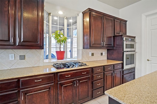 kitchen with backsplash, light tile patterned flooring, light stone counters, and stainless steel appliances