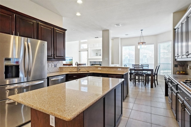 kitchen featuring appliances with stainless steel finishes, sink, a tile fireplace, pendant lighting, and a kitchen island