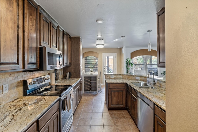 kitchen with backsplash, sink, hanging light fixtures, appliances with stainless steel finishes, and light stone counters