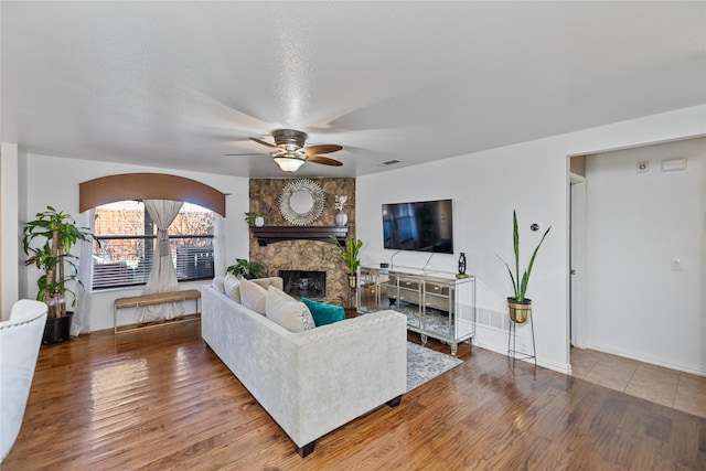 living room featuring hardwood / wood-style floors, ceiling fan, a fireplace, and a textured ceiling