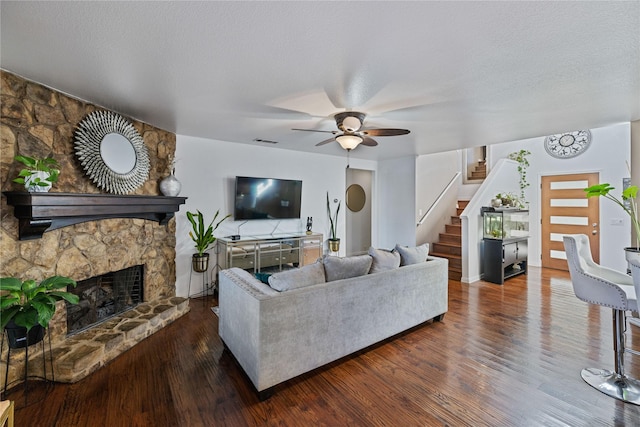 living room featuring ceiling fan, a stone fireplace, dark hardwood / wood-style flooring, and a textured ceiling