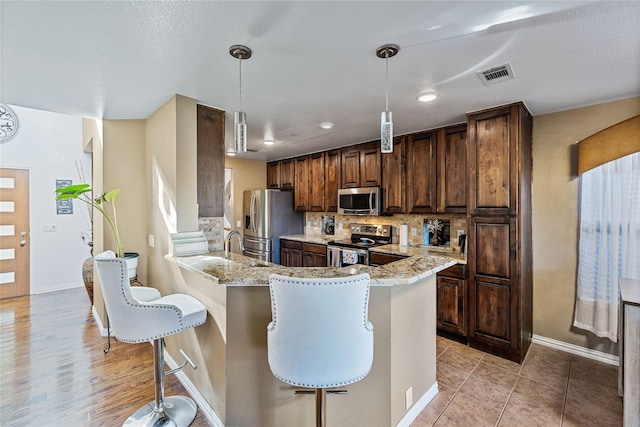 kitchen featuring backsplash, decorative light fixtures, light stone counters, kitchen peninsula, and stainless steel appliances