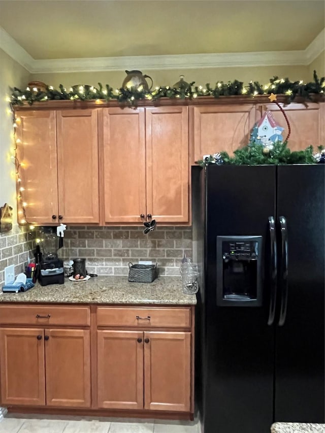 kitchen featuring light stone countertops, backsplash, black fridge with ice dispenser, crown molding, and light tile patterned floors