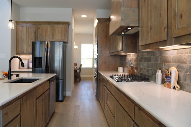 kitchen with sink, stainless steel appliances, pendant lighting, light hardwood / wood-style floors, and exhaust hood