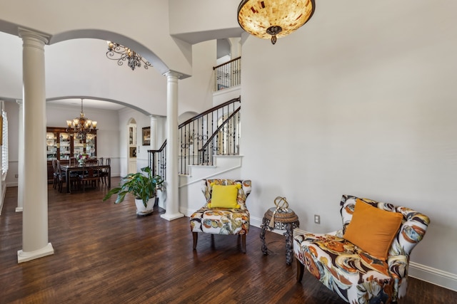 entrance foyer featuring decorative columns, a towering ceiling, dark wood-type flooring, and a notable chandelier