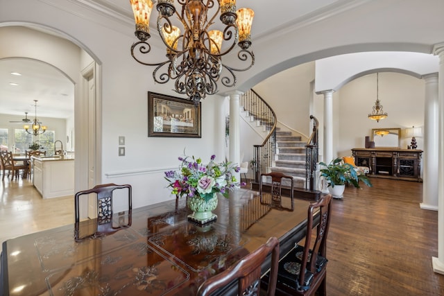 dining space featuring sink, hardwood / wood-style flooring, ornamental molding, a notable chandelier, and decorative columns