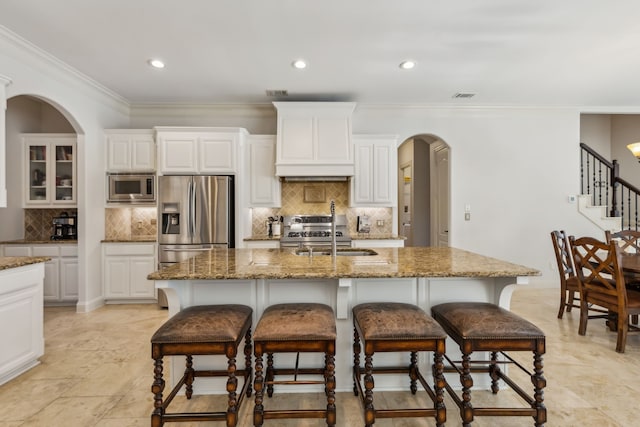 kitchen featuring stone counters, an island with sink, stainless steel appliances, and custom range hood