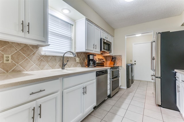 kitchen with white cabinets, appliances with stainless steel finishes, sink, and washing machine and clothes dryer