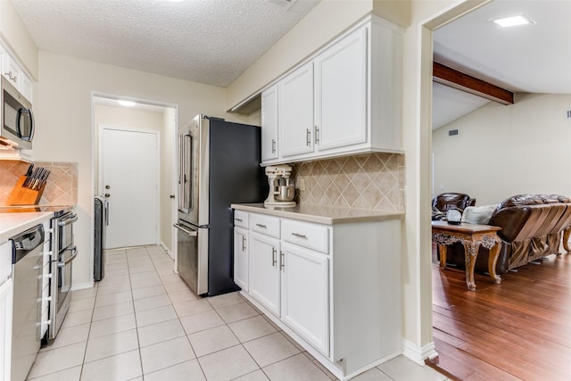 kitchen with lofted ceiling with beams, a textured ceiling, white cabinets, stainless steel appliances, and backsplash