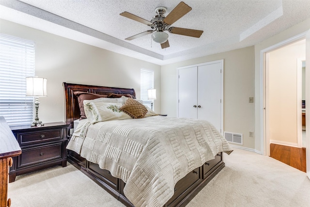 bedroom featuring ceiling fan, a closet, light carpet, and a textured ceiling