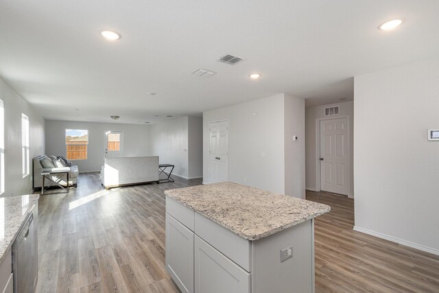 kitchen featuring light stone countertops, light wood-type flooring, dishwasher, white cabinets, and a kitchen island