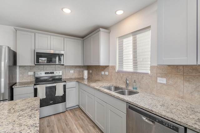 kitchen with light stone countertops, light wood-type flooring, stainless steel appliances, sink, and white cabinetry