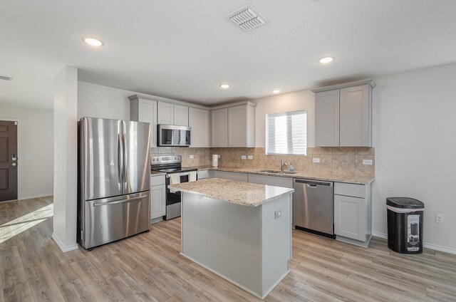 kitchen featuring sink, a center island, stainless steel appliances, light stone counters, and light wood-type flooring