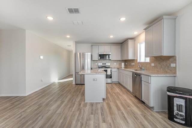 kitchen featuring light stone countertops, appliances with stainless steel finishes, gray cabinets, a kitchen island, and light wood-type flooring