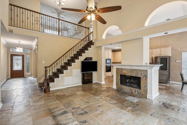 unfurnished living room featuring a fireplace, a towering ceiling, ceiling fan, and crown molding